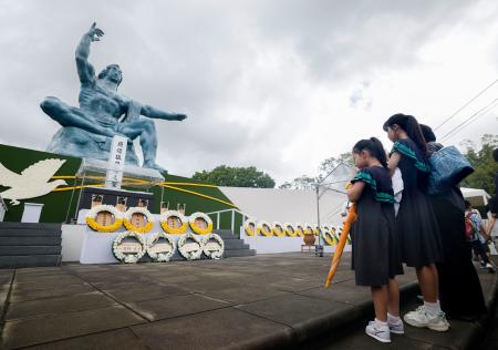 　長崎市の平和公園を訪れ、平和祈念像の前で手を合わせる女の子ら＝９日午後