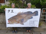 釣り上げたクエの魚拓を持つ山内省二さん（右）と妻幸子さん＝鹿児島市桜ケ丘６丁目