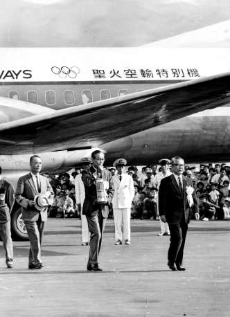 寺園知事の先導で聖火灯が到着。後方のYS11の機体には五輪マークと「聖火空輸特別機」の文字が見える＝1964年9月9日