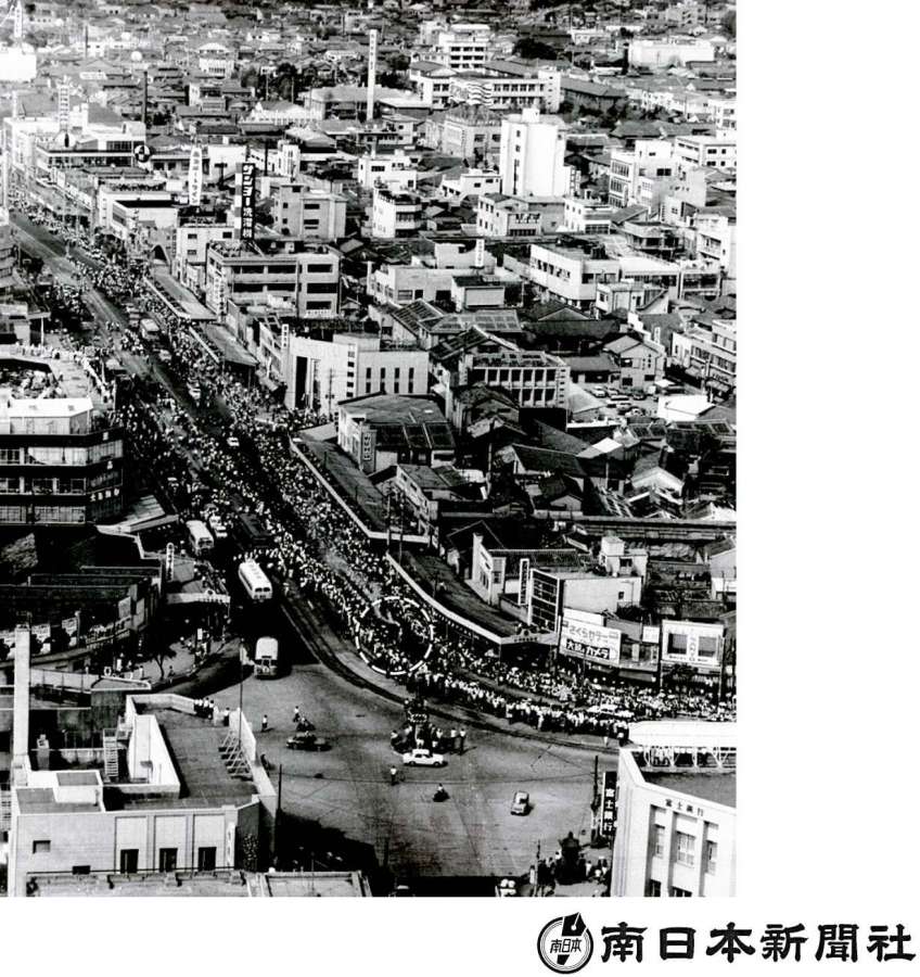 市街地中心部を走る聖火。道路の両脇には人垣が連なる＝1964年9月9日、鹿児島市のいづろ通り