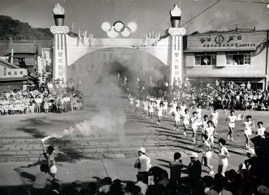白煙をたなびかせ県庁前を出発する聖火リレー＝1964年９月１０日、鹿児島市山下町