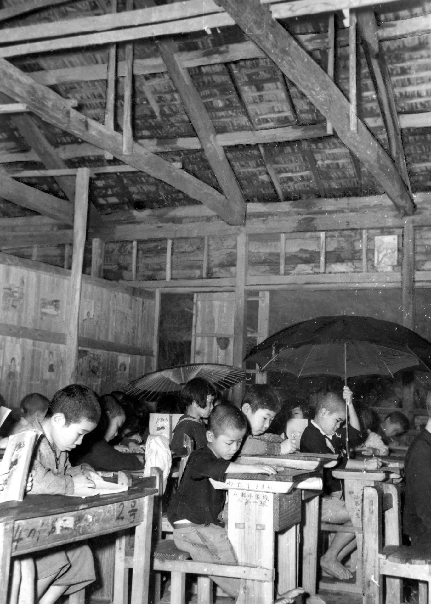 雨漏りのする校舎で傘を差して勉強する名瀬小学校の子どもたち＝１９５２（昭和２７）年１２月１日