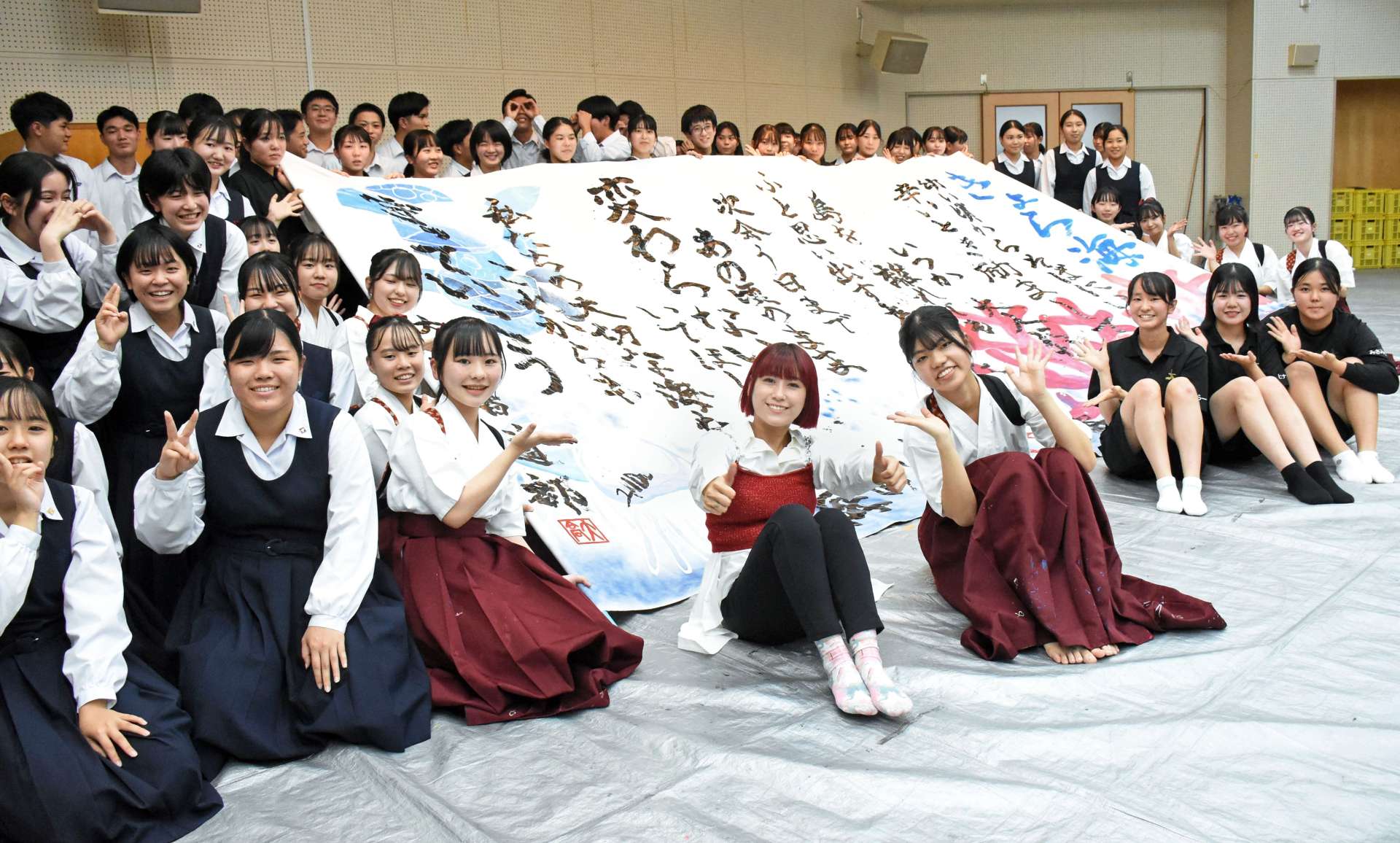 １１８番通報を啓発する作品の前で記念写真に収まるＩＭＡＬＵさん（中央）＝奄美市名瀬の大島高校