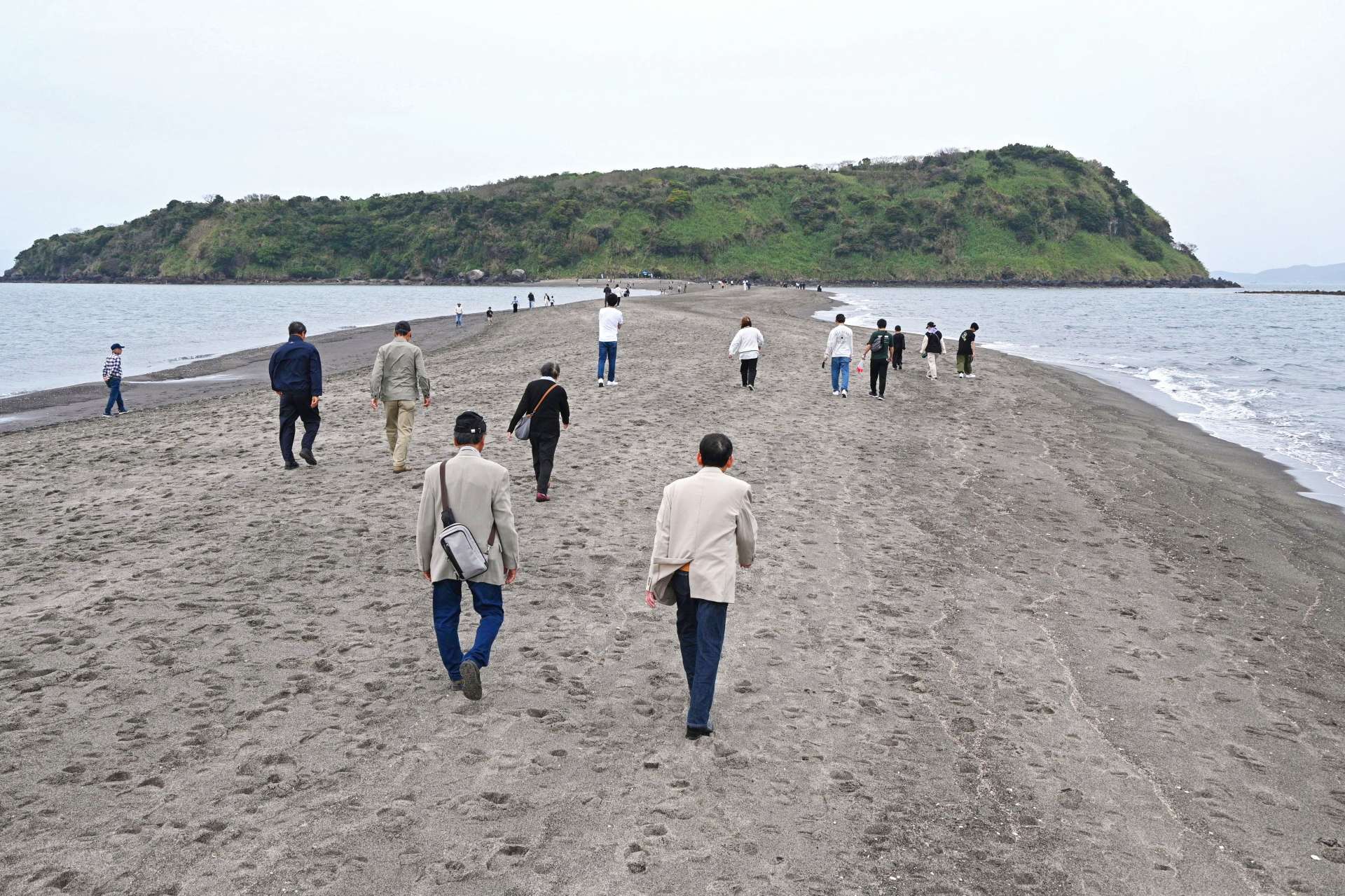 引き潮で出現した砂州を知林ケ島に向かって歩く人たち＝３０日午後３時１０分、指宿市東方