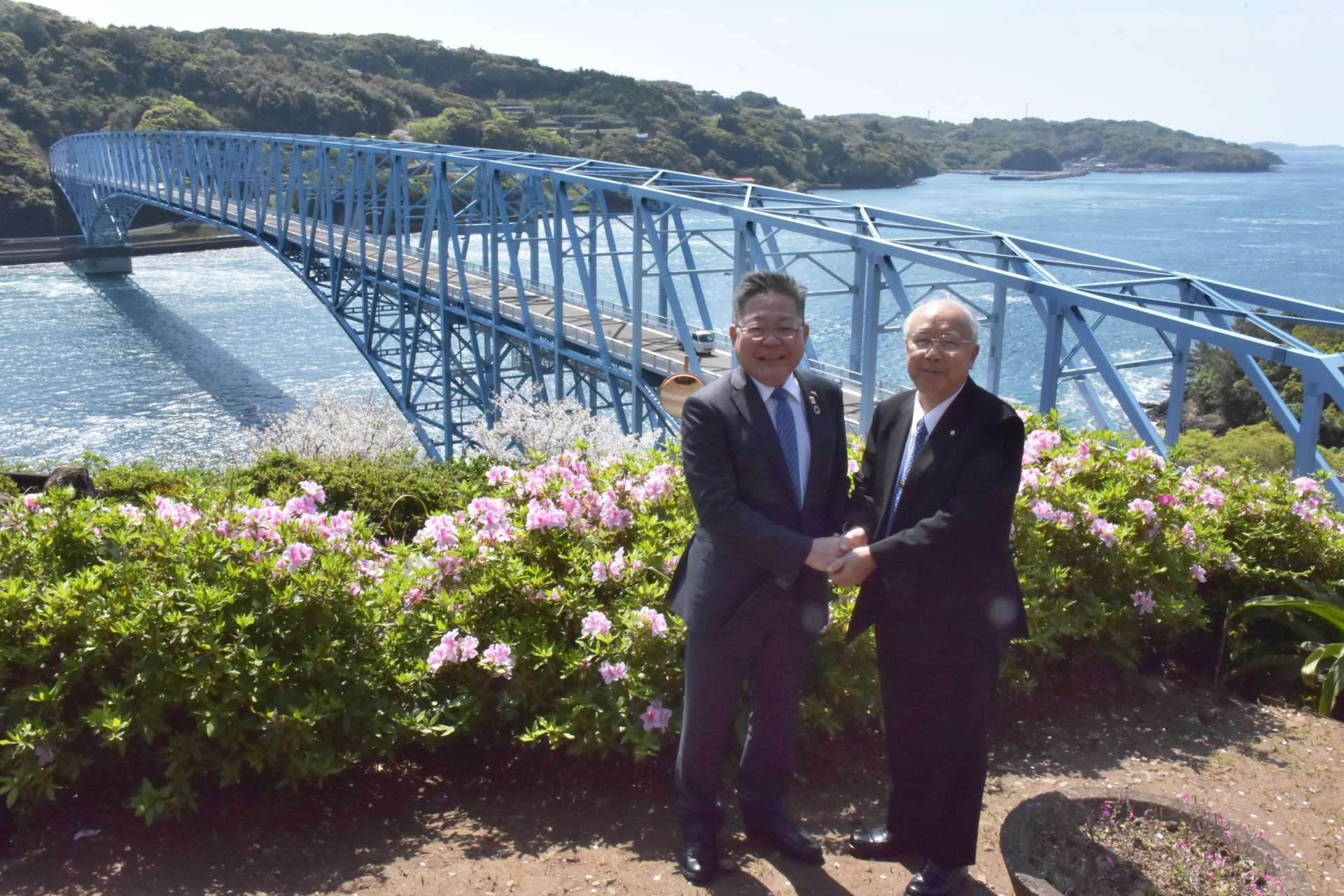 黒之瀬戸大橋を見下ろす展望所で、手を取り合う西平良将・阿久根市長（左）と川添健・長島町長＝９日、長島町山門野のうずしおパーク
