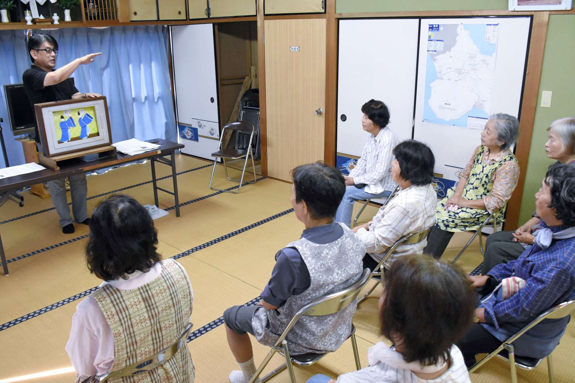 紙芝居を通し、地元住民に立て札刷新の趣旨を説明する石堂秀一さん＝指宿市開聞