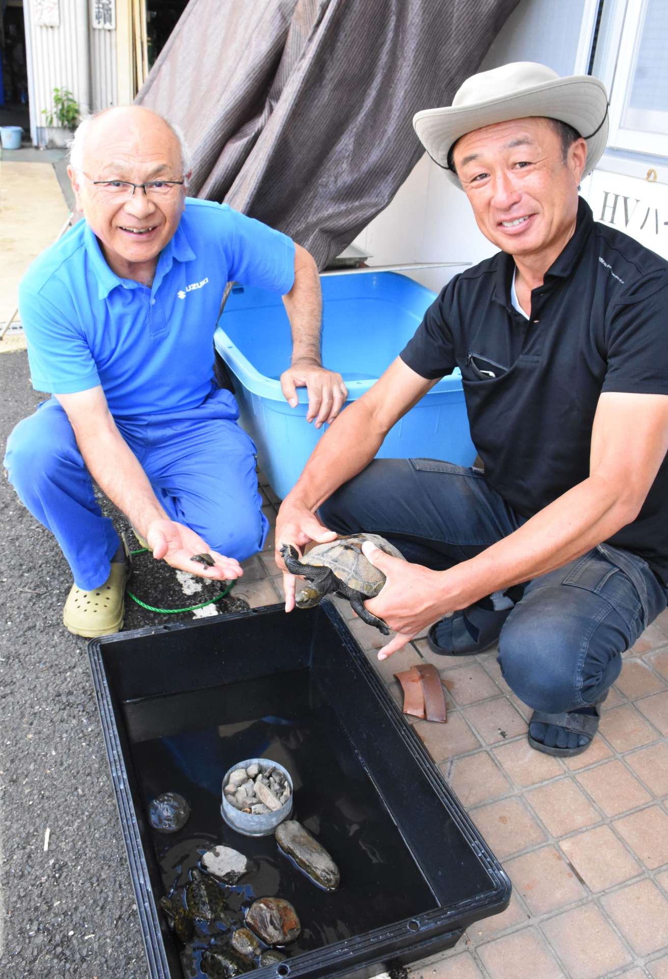 生まれたばかりのニホンイシガメを前に、笑顔を見せる川口正樹さん（左）と岩切俊巳さん＝指宿市十町