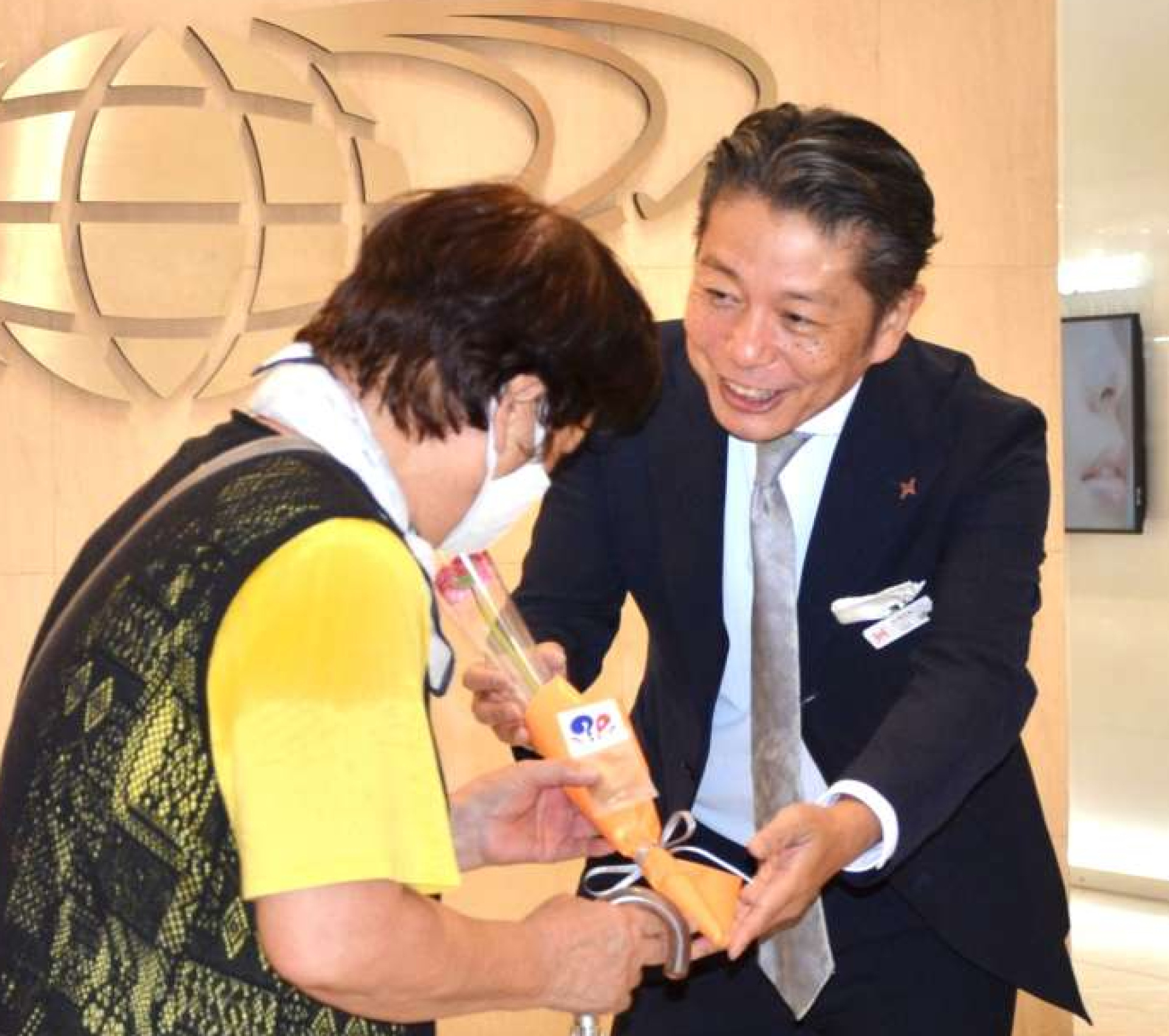 アミュプラザ鹿児島開業２０周年を記念し、来館者に花束を渡すＪＲ鹿児島シティの山崎慎介社長（中央）＝１７日、鹿児島市
