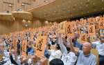 「道」と書かれたボードを掲げ、国道２２２号牛ノ峠バイパス未着工区間の再事業化を求める大会決議を採択する参加者＝２１日、都城市総合文化ホール