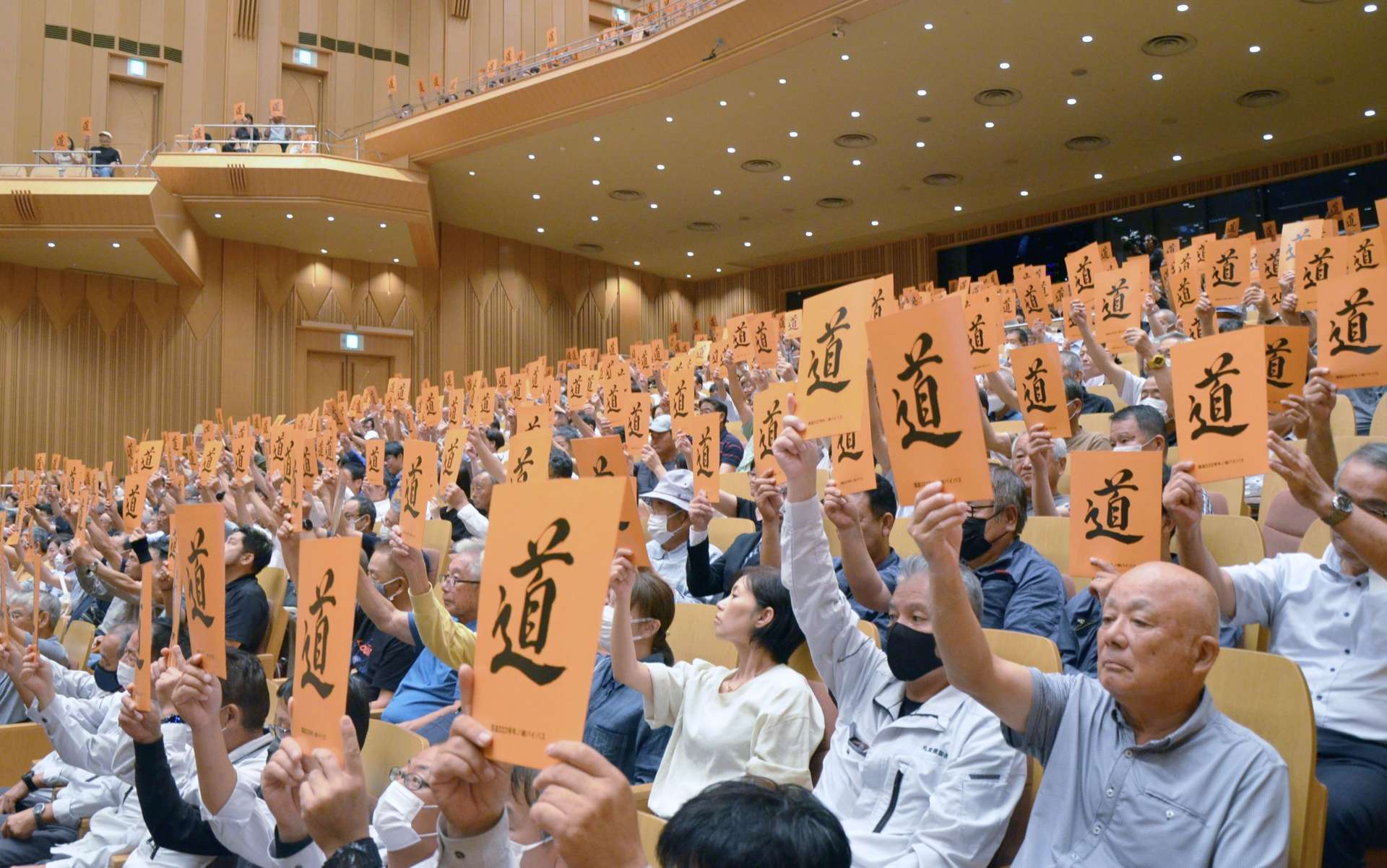 「道」と書かれたボードを掲げ、国道２２２号牛ノ峠バイパス未着工区間の再事業化を求める大会決議を採択する参加者＝２１日、都城市総合文化ホール