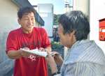 笑顔で新聞を配る川畑兼吾さん（左）＝薩摩川内市上甑町平良
