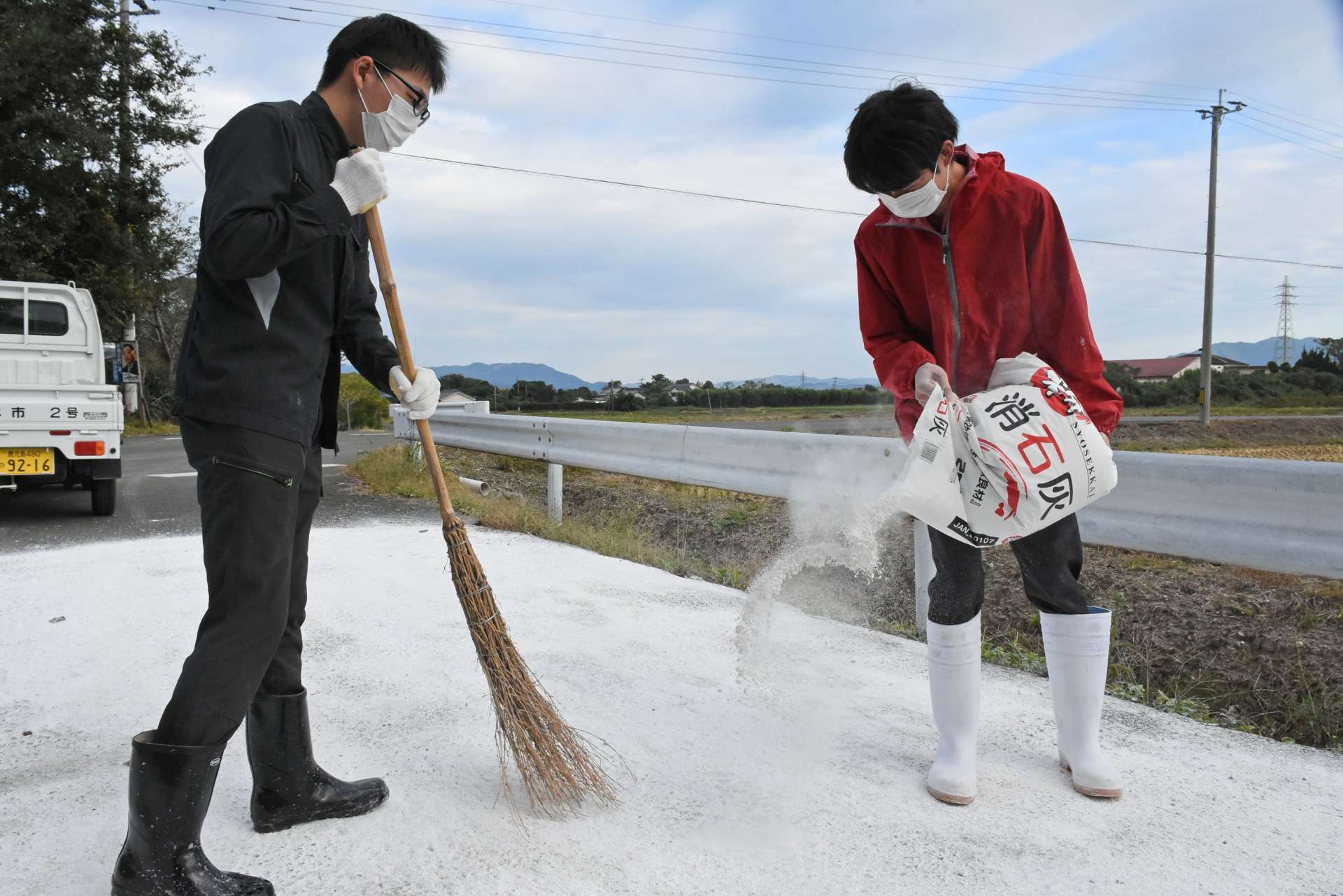 道路に消石灰をまく出水市職員＝８日午後、同市高尾野町下水流
