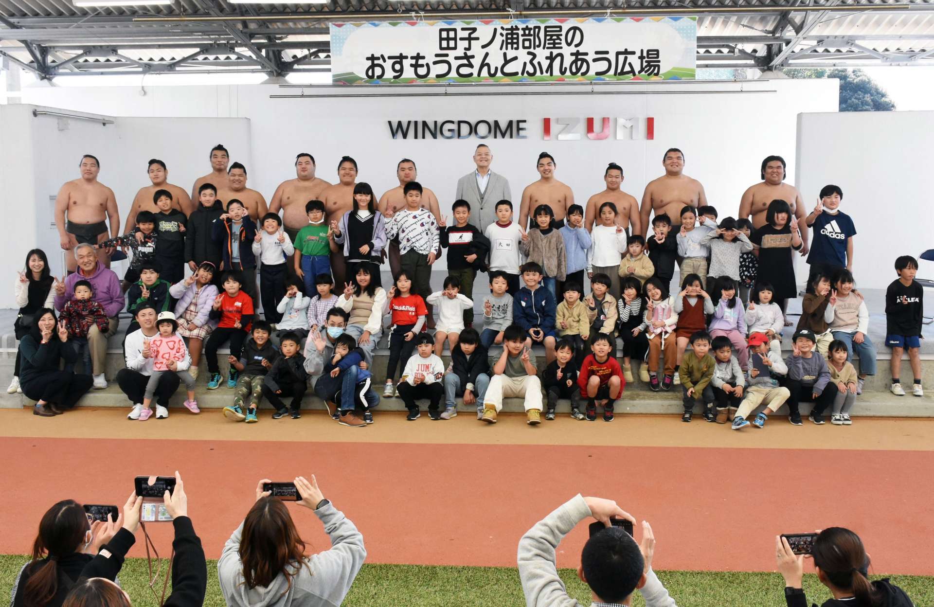 田子ノ浦親方（後列右から５人目）や力士と記念撮影する子どもら＝出水市のウイングドームいずみ