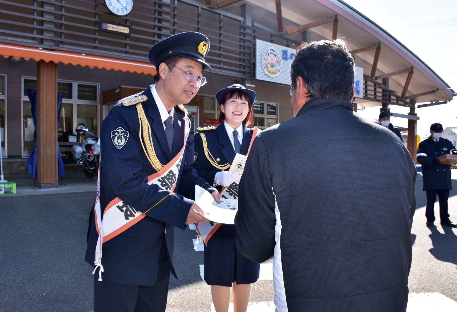 一日署長に任命され、１１０番の適正利用を呼びかける乾き亭げそ太郎さん（左）と久木崎みなみさん（中）夫妻＝長島町の道の駅「黒之瀬戸だんだん市場」