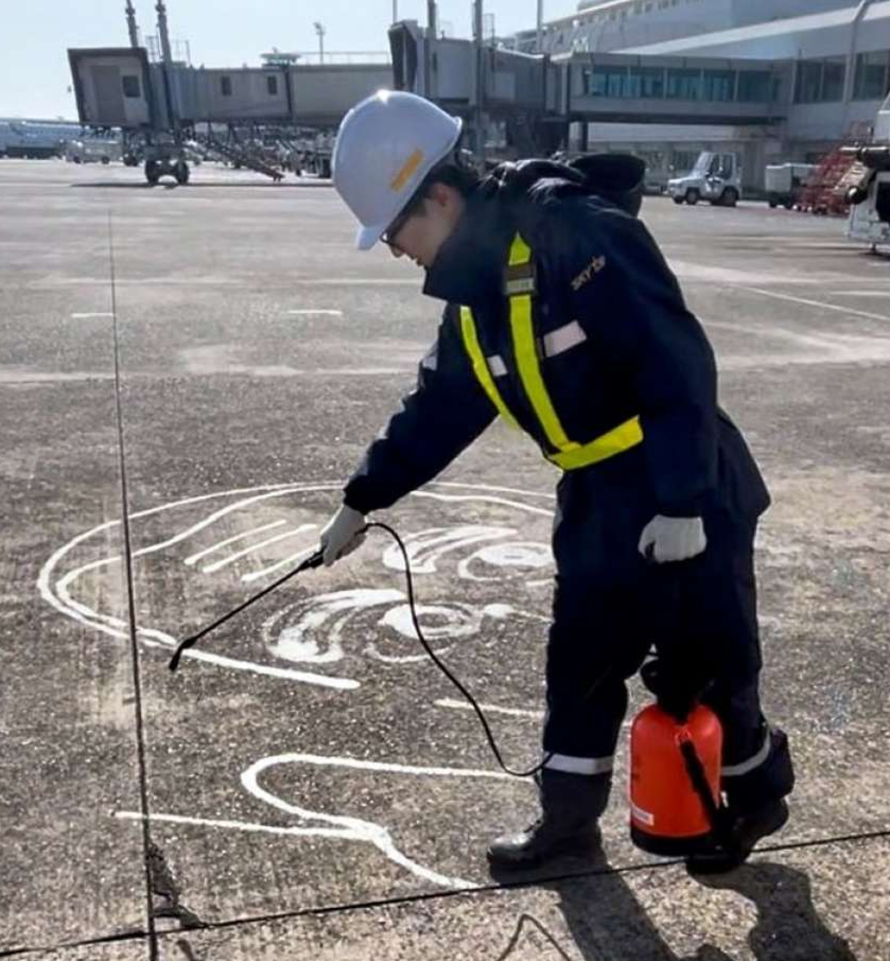 噴霧器を使い駐機場に西郷隆盛のイラストを描く三角真生さん＝霧島市溝辺の鹿児島空港