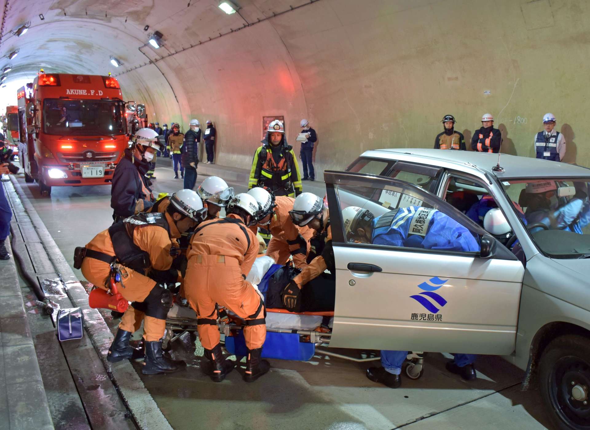 事故車両に閉じ込められた負傷者を協力して運び出す阿久根市と薩摩川内市の消防職員ら＝２０日、阿久根市鶴川内の横座トンネル