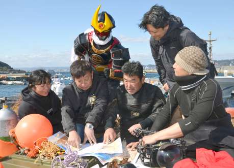 薩摩剣士隼人とともに、桜島沖の調査地点を地図で確認する「チェスト探検隊」の外山雄大隊長（左から２人目）＝鹿児島市桜島赤生原町
