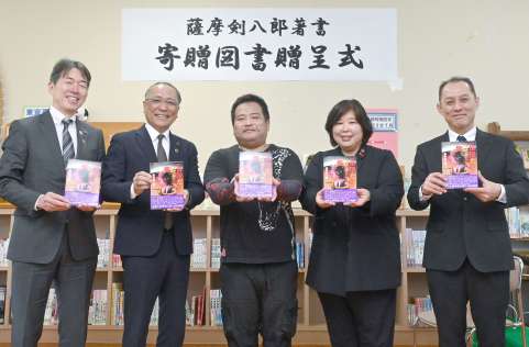 薩摩剣八郎さんの図書寄贈を喜ぶ出水市の関係者。中央が潟山類さん＝同市の江内中学校