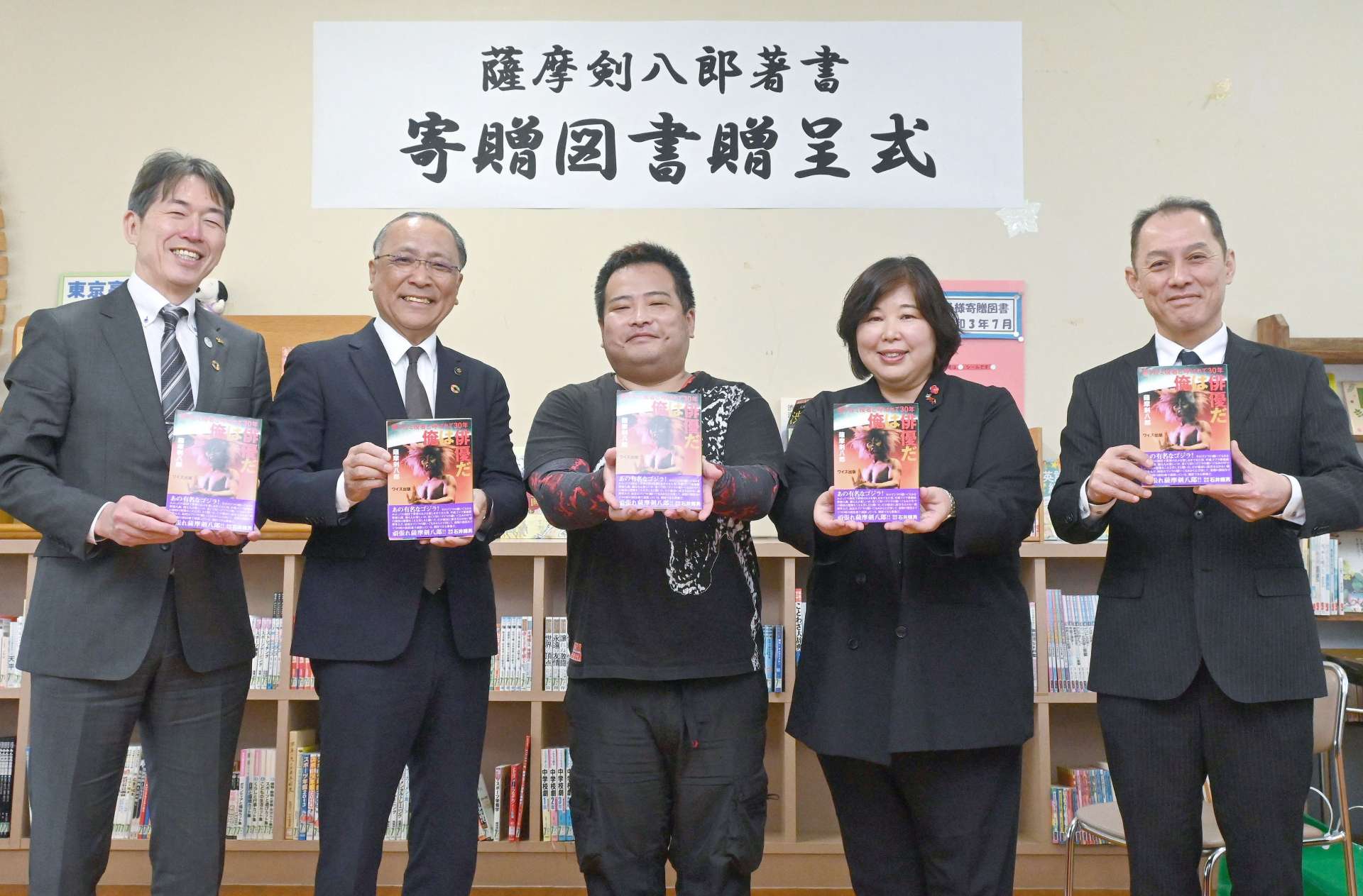薩摩剣八郎さんの図書寄贈を喜ぶ出水市の関係者。中央が潟山類さん＝同市の江内中学校