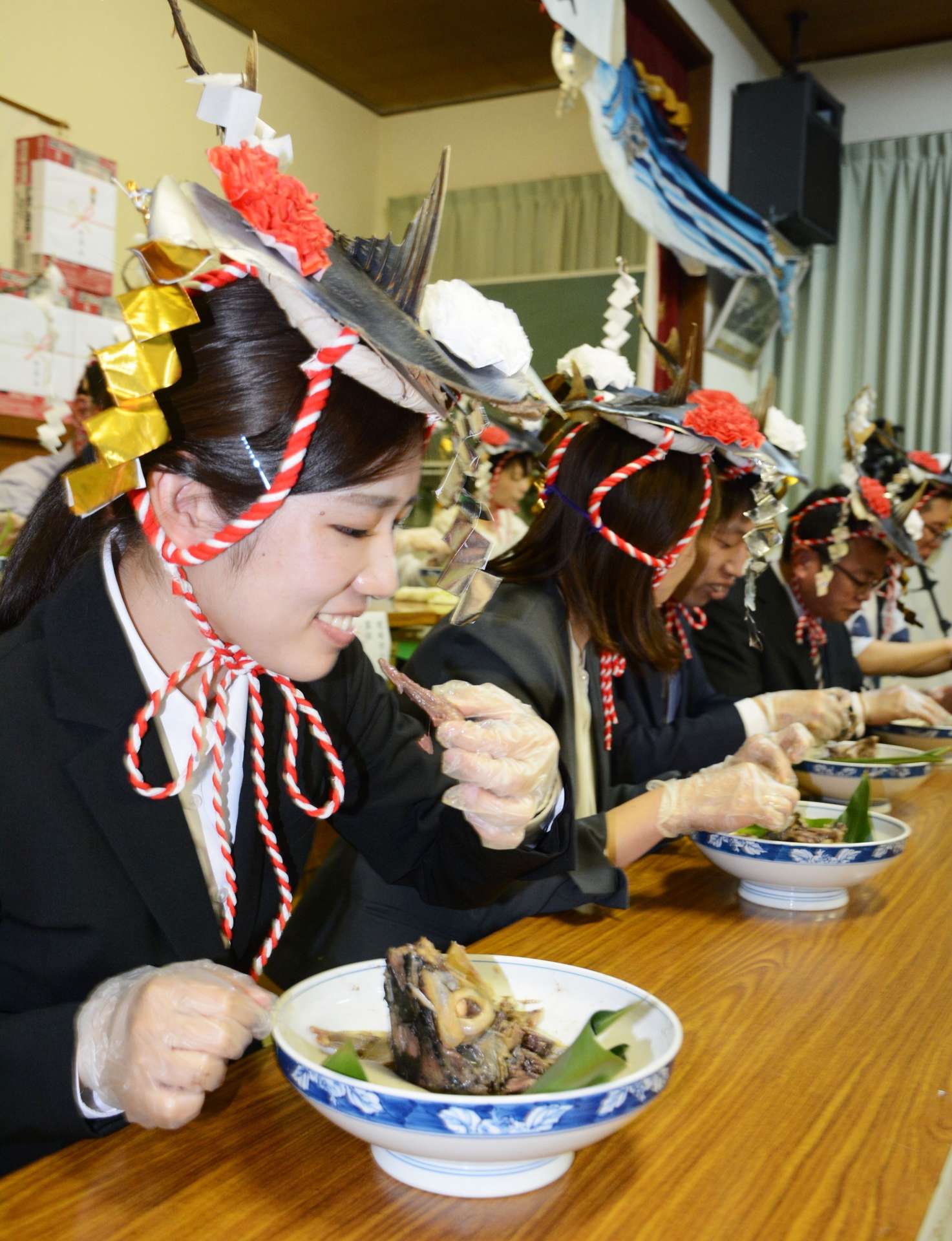 カツオのビンタ料理を手づかみで食べる教員＝１１日夜、枕崎市の大塚公民館
