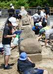 腹ばいになって砂の彫刻に挑む子どもたち＝１９日、南さつま市加世田麓町
