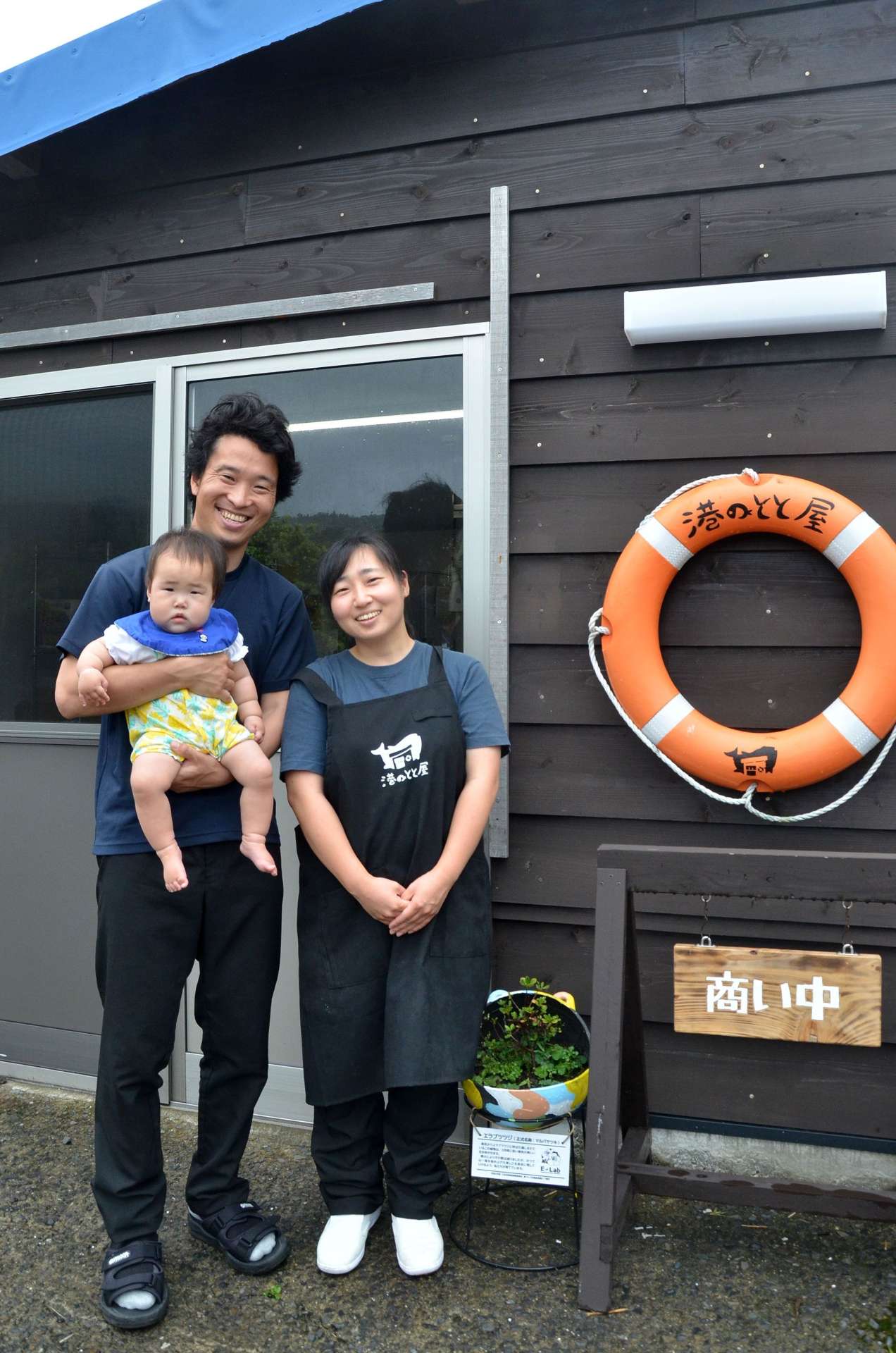 自分たちで建てた水産加工店の前に立つ池添慧さん、晴香さん夫妻と青ちゃん