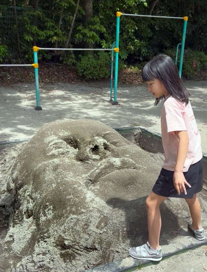 砂場に突然現れた巨大な顔。細部まで精巧に作られている＝１日、鹿児島市明和３丁目