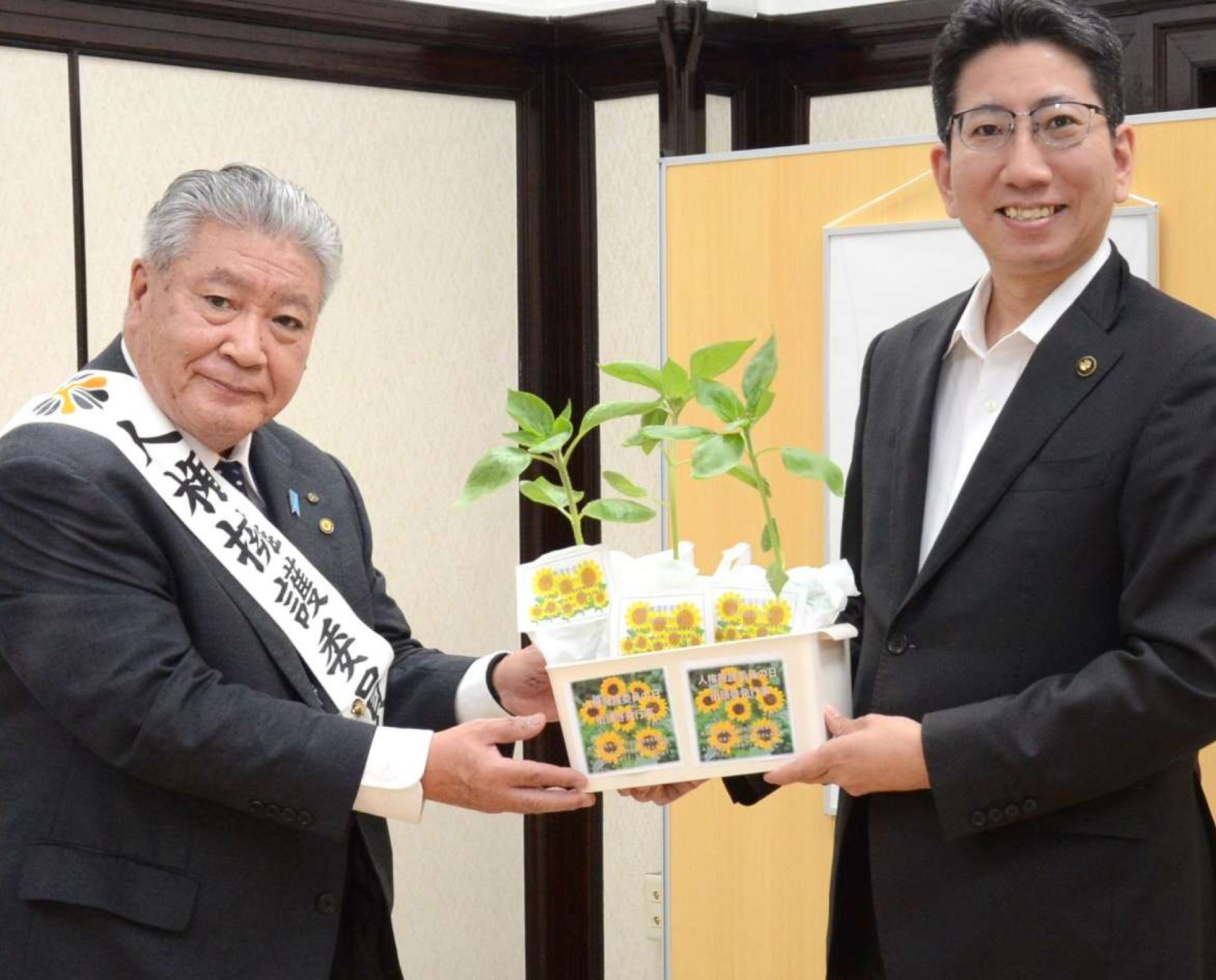 下鶴隆央市長にヒマワリの苗を贈る鹿児島人権擁護委員協議会の口羽勝法会長＝２日、鹿児島市役所