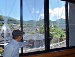 飛散防止のテープを貼った窓から新燃岳の噴煙を眺める児玉昇館長＝２８日、霧島市牧園の高千穂地区公民館