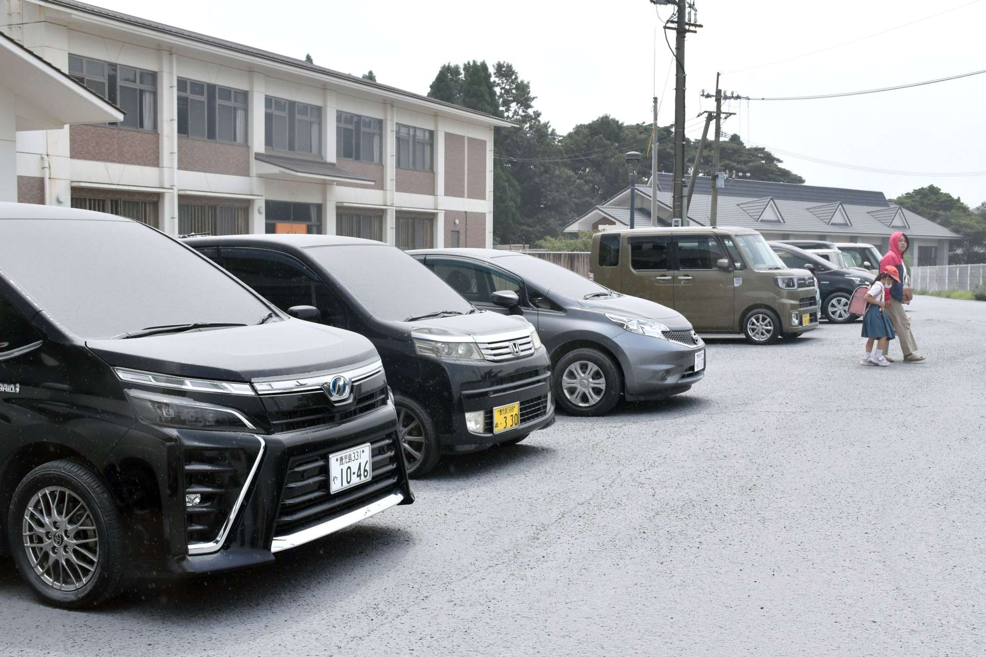 灰が降る中、児童を迎えに来た保護者＝２日午後１時５５分、霧島市牧園の高千穂小学校