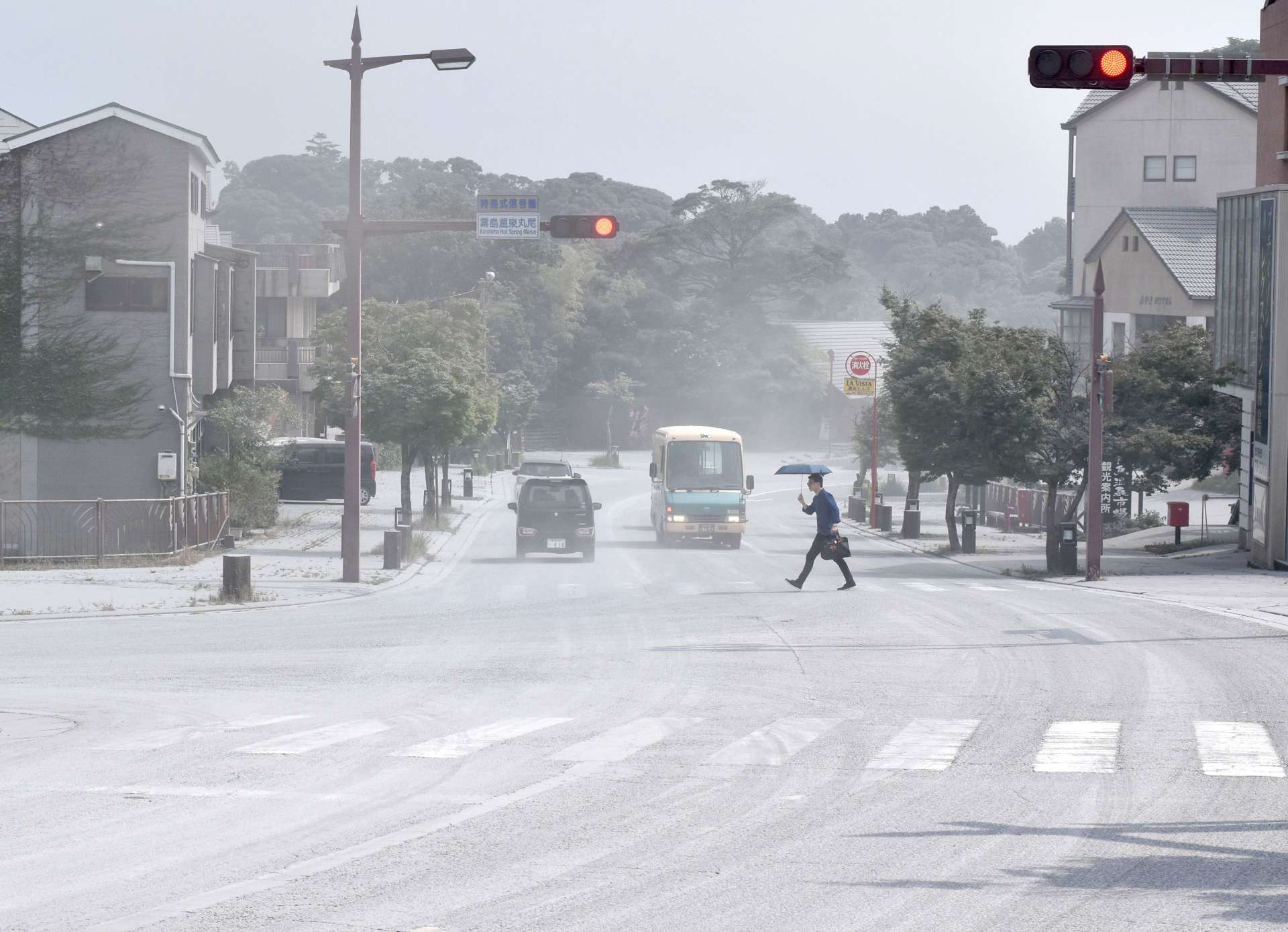 降灰の中、傘を差して横断する人や行き交う車＝２日午後２時４５分ごろ、霧島市牧園町高千穂