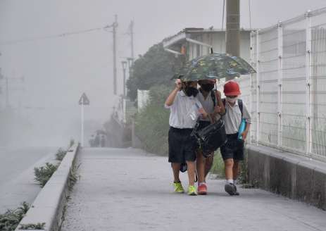 〈降り続ける灰〉灰を避けようと、一つの傘に入り下校する子どもたち＝３日午後３時半ごろ、霧島市牧園町高千穂