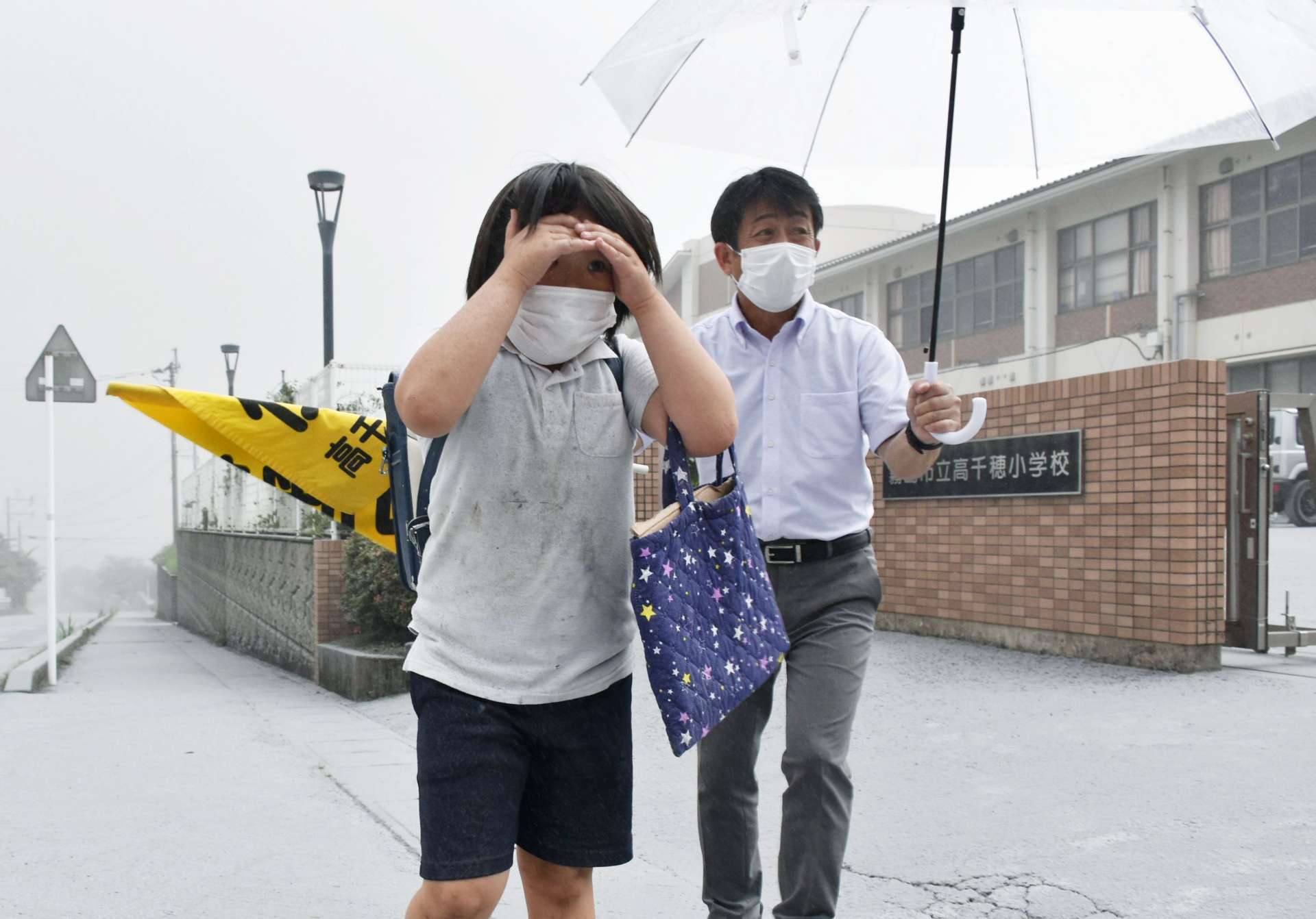 目元を手で覆い、灰が入らないようにして下校する児童＝３日午後３時２５分ごろ、霧島市牧園町高千穂の高千穂小学校