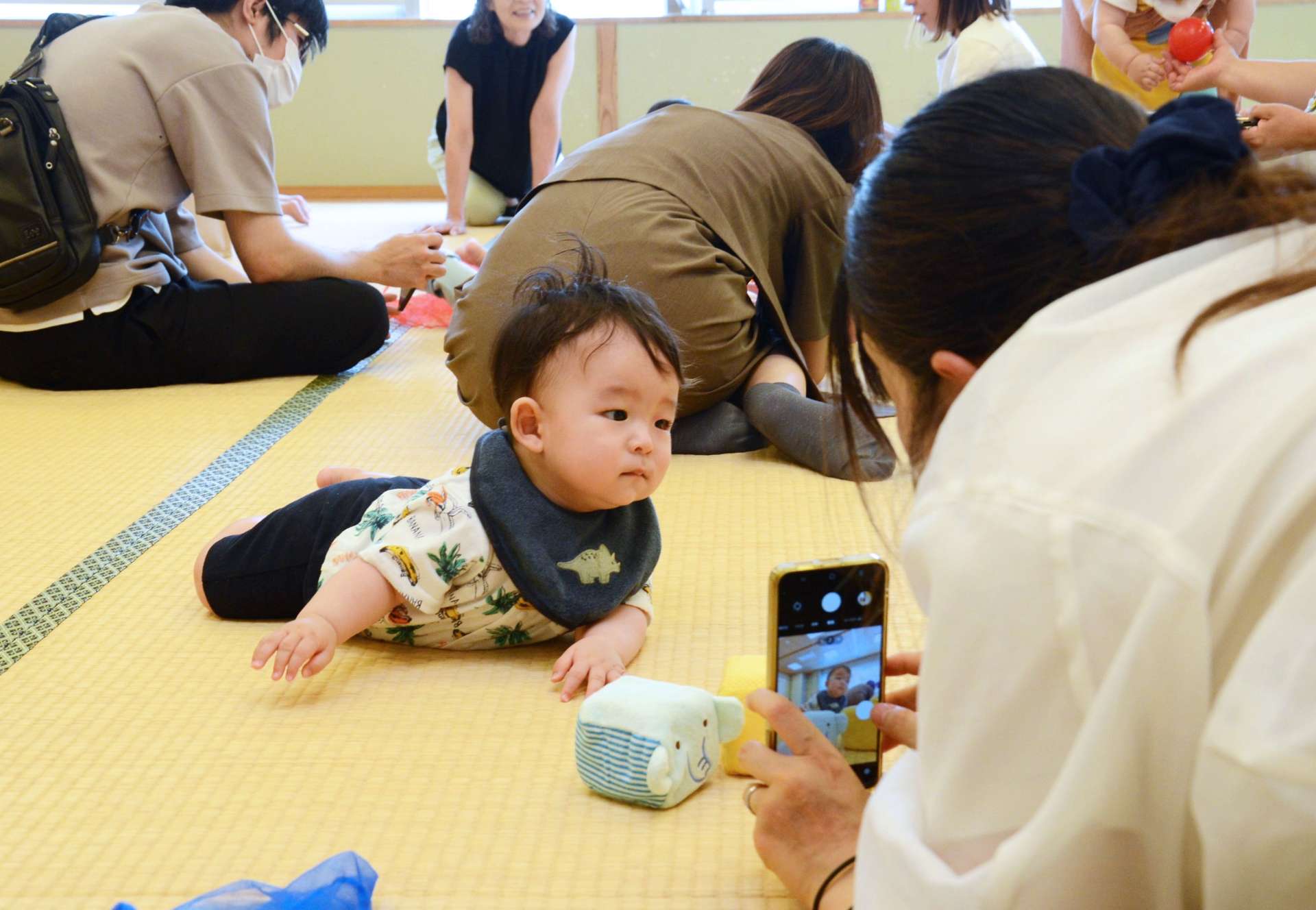 赤ちゃんの一瞬の表情を捉えようと奮闘する参加者＝３日、鹿児島市東部親子つどいの広場なかまっち