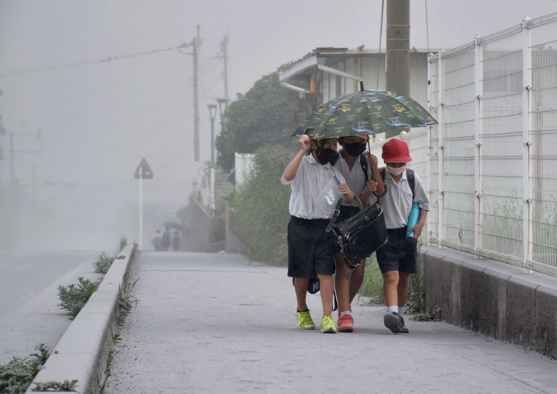 灰が降る中、一つの傘に入り下校する子どもたち＝３日午後３時半ごろ、霧島市牧園町高千穂