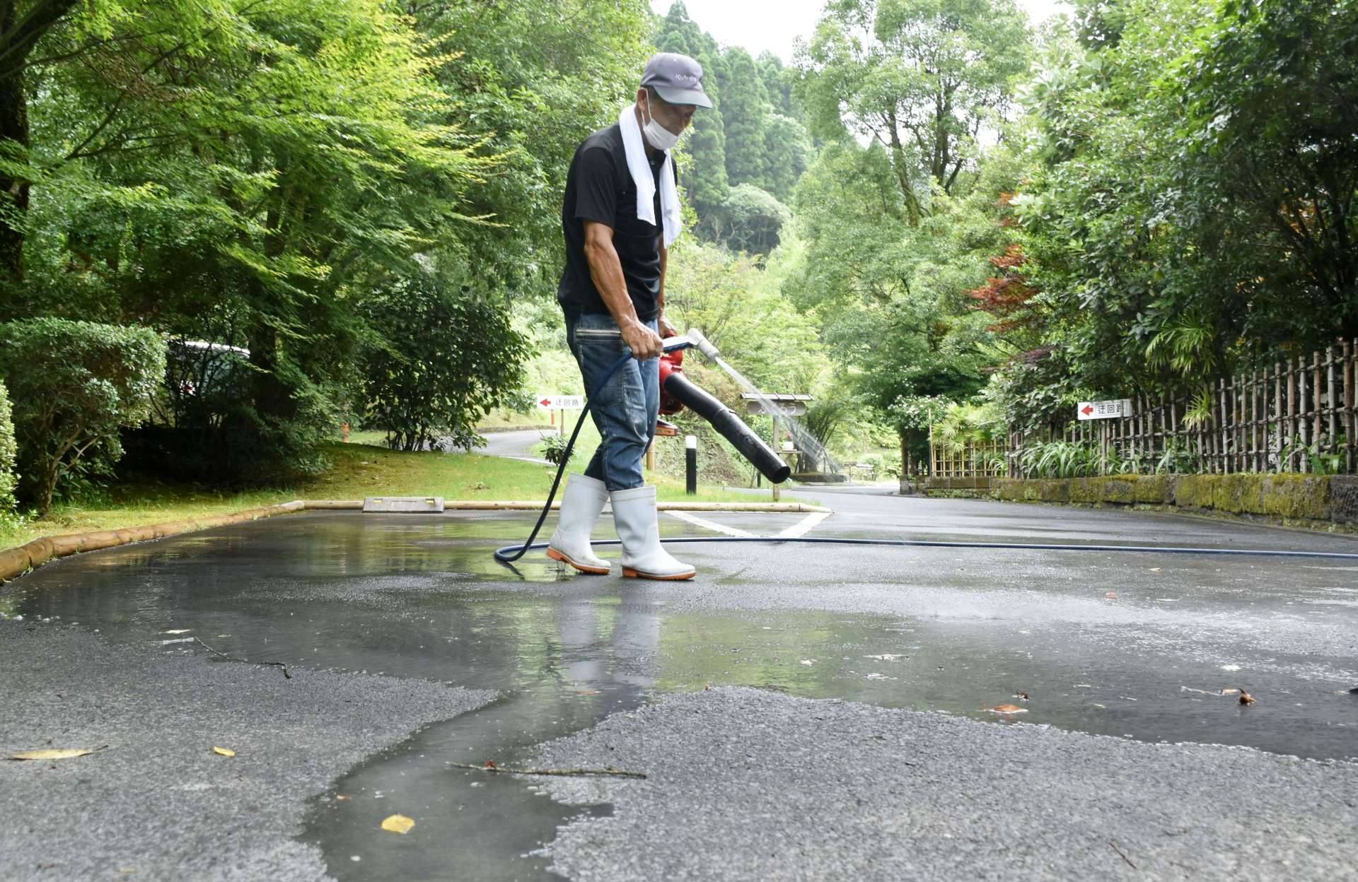 灰が積もった路面を水とブロワーで洗い流す従業員＝５日、霧島市牧園町中津川のおりはし旅館