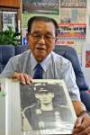 父・栄助さんの遺影を手に「苦しんでいる父に何もしてやれなかった」と振り返る神村勲さん＝いちき串木野市の神村学園