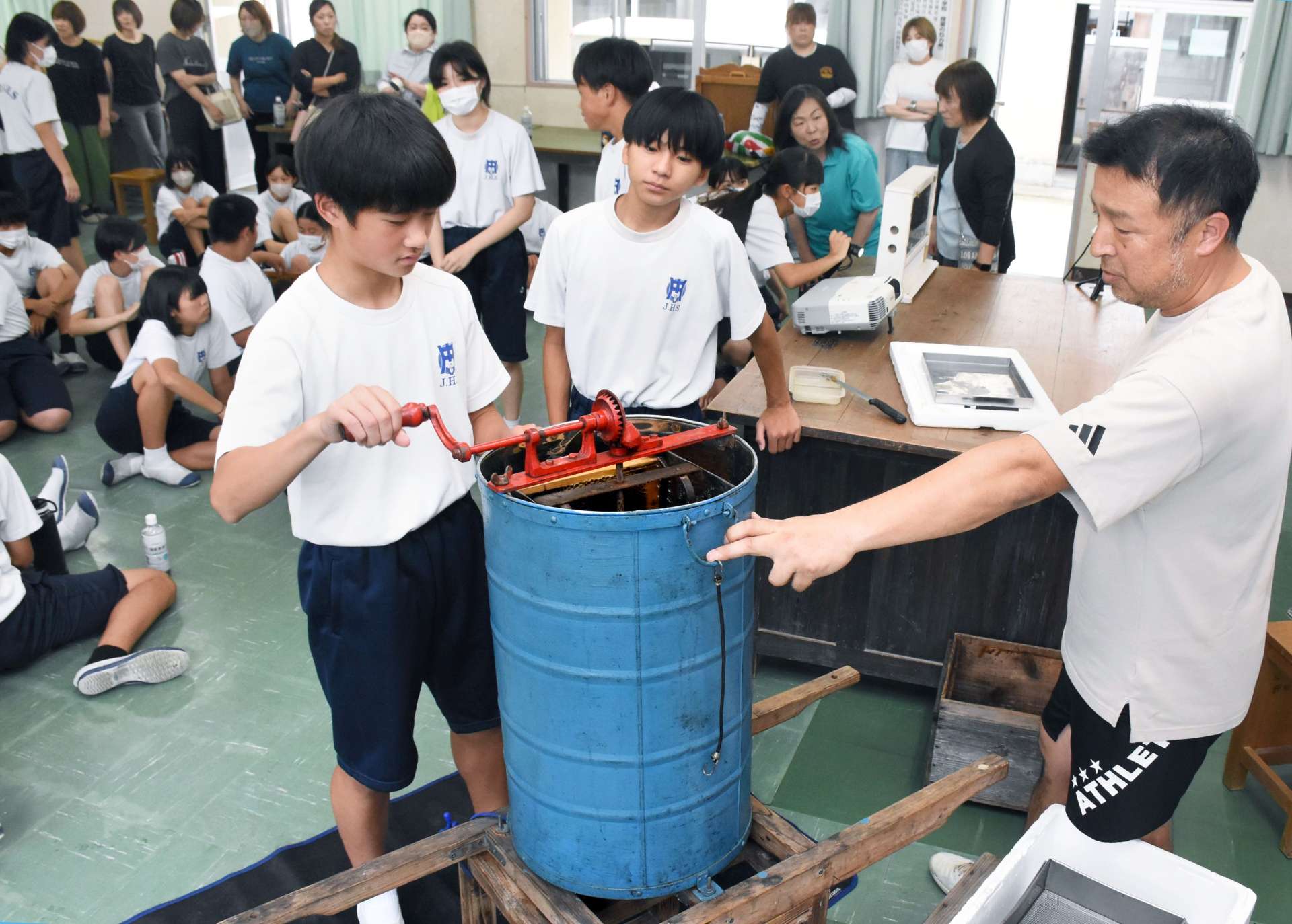 巣を遠心分離機にかけてハンドルを回す生徒たち＝出水市の野田中学校