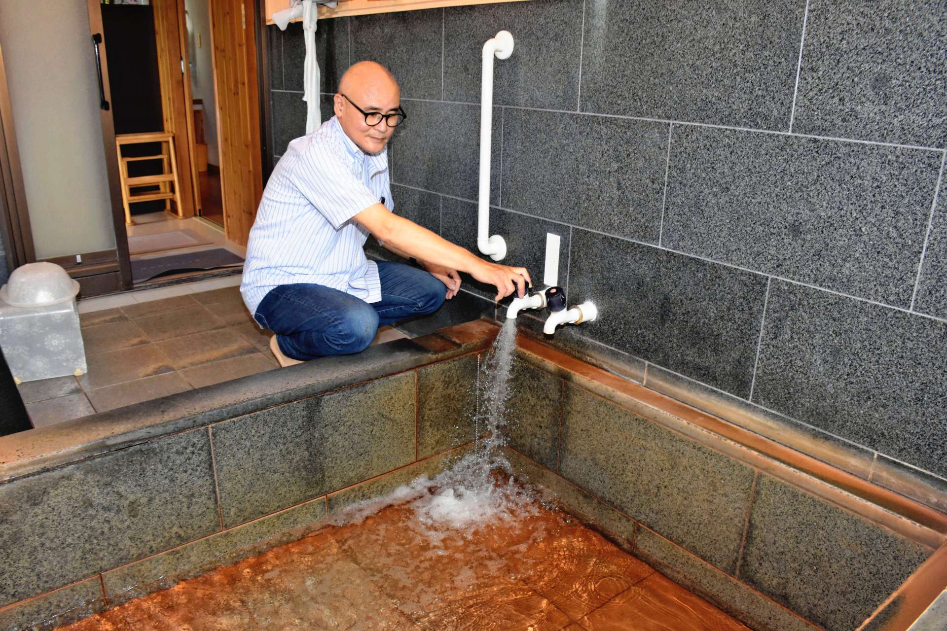 自宅で配湯サービスを利用する原口貞輝さん。風呂場の蛇口をひねると、勢いよく温泉水が流れ出した＝指宿市西方