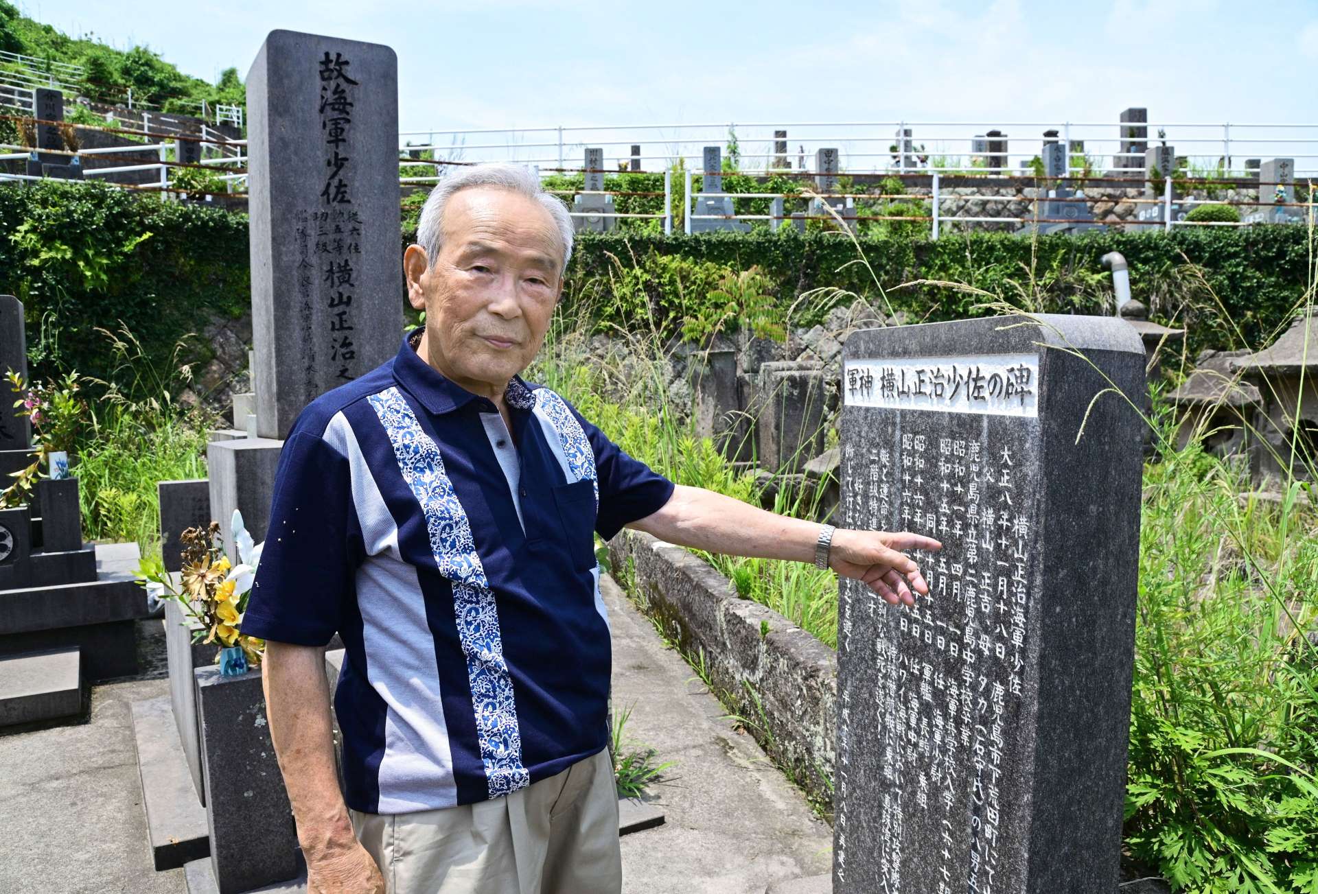 「軍神　横山正治少佐の碑」前に立つ横山正照さん＝７月５日、鹿児島市郡元町