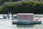 西京ダムに浮かぶ「ピンクの鯨」。奥で水中装置点検のためダイバーが飛び込む＝西之表市