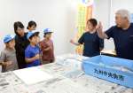 指で値段を示す競りの仕方を教わる親子＝鹿児島市中央卸売市場魚類市場