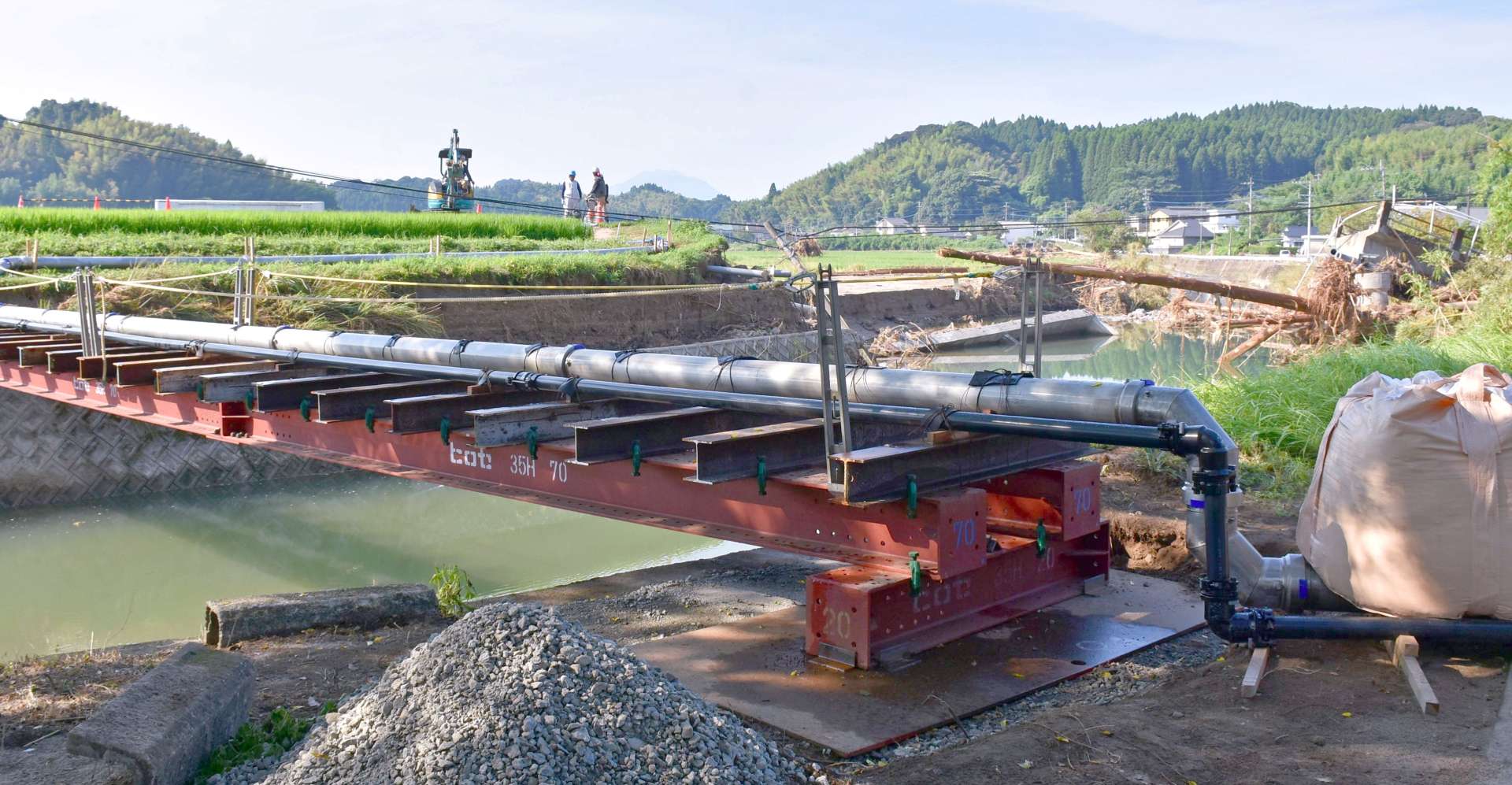 中田橋（右奥）の崩落に伴い破損した配水管の仮設工事を終えた現場＝１５日、姶良市加治木町小山田