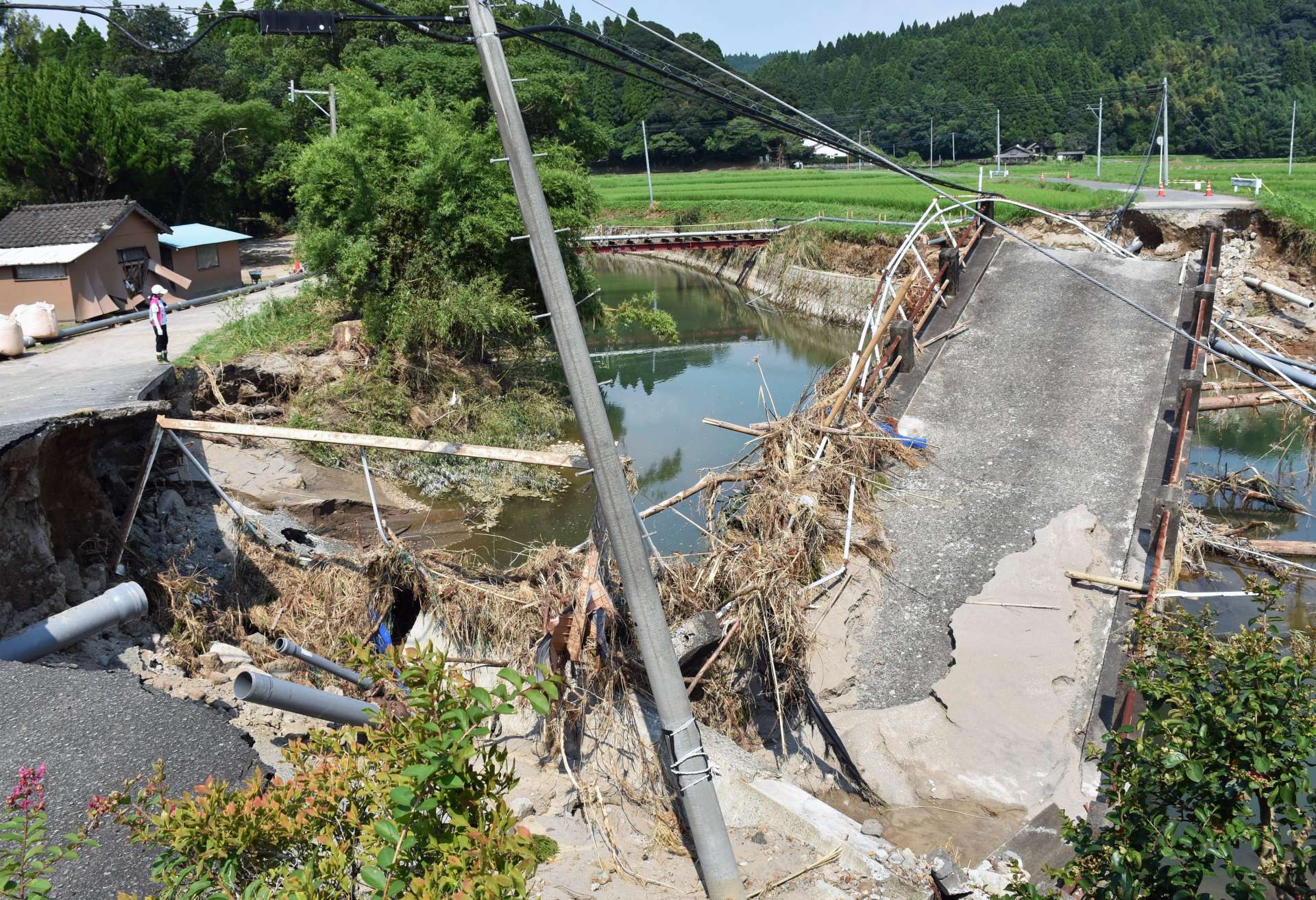 〈大雨で崩落した中田橋〉脱落した送水管の仮設工事が１４日完了した（写真奥で川を渡り左側に延びる）＝１５日、姶良市加治木町小山田