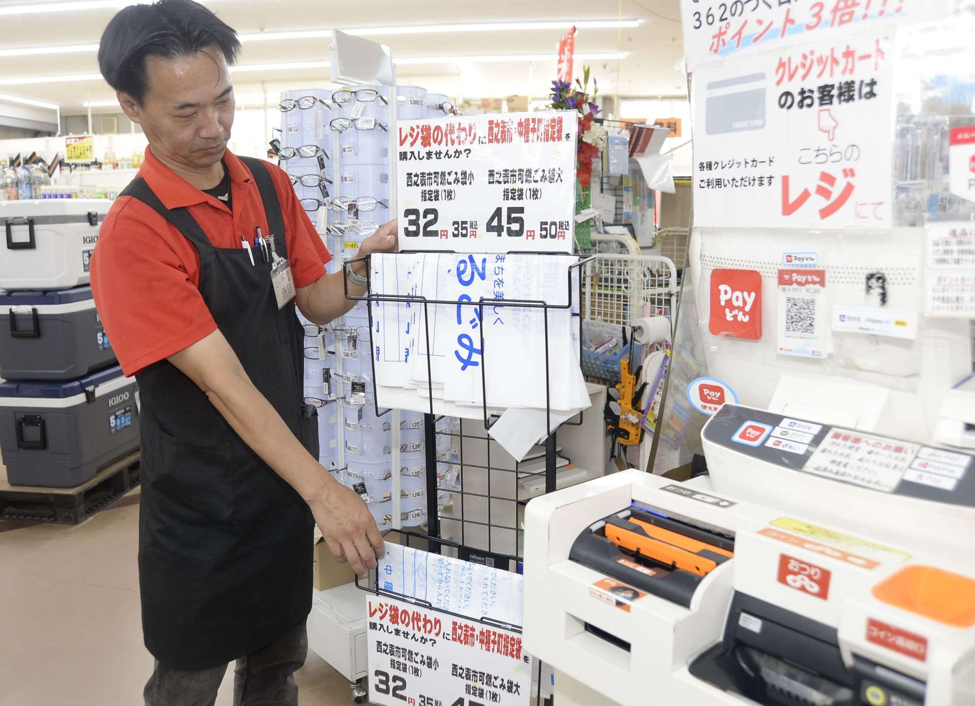 レジ横にばら売りの指定ごみ袋を陳列する店員＝西之表市のサムズ西之表店