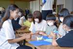 一緒に折り紙で遊ぶ留学生（左）と子どもたち＝いちき串木野市の大原交流センター