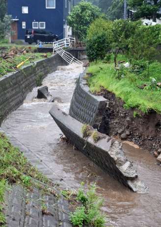 〈再びの激しい雨で倒壊寸前〉８日の大雨で崩れた護岸が倒れそうな枦山川＝２１日午後４時半、姶良市平松