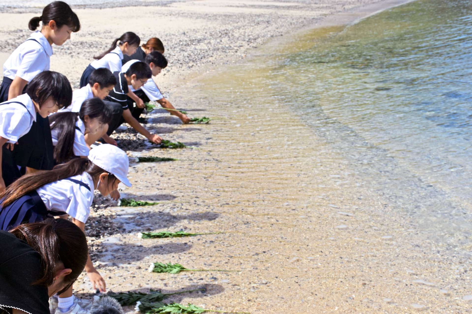 多くの遺体が流れ着いた船越海岸で献花する子どもたち＝２４日、宇検村