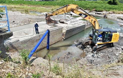 農業用取水施設が流出した現場で、水田に水を供給するための仮設の給水管を設置する工事関係者ら＝２５日午前１１時４０分、姶良市深水