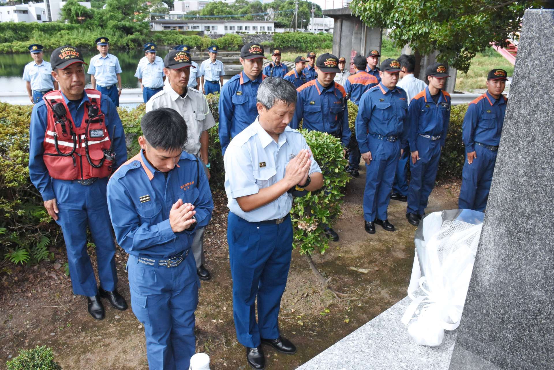 戸崎和弘さんの慰霊碑に手を合わせる消防職員＝出水市上鯖渕